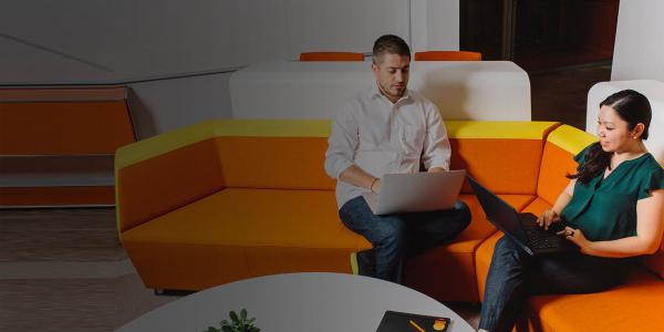 colleagues-using-laptops-on-orange-couch-1300x650