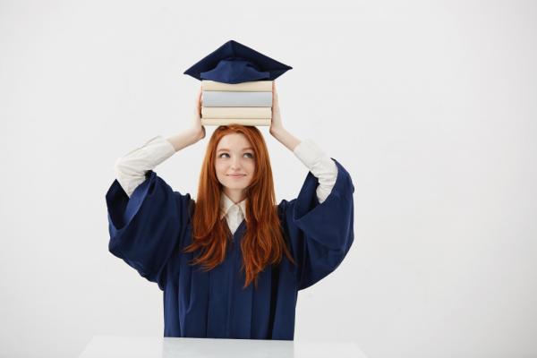 ginger-woman-graduate-mantle-smiling-holding-books-head-cap